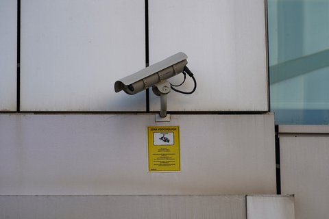 Cámara de videovigilancia en la fachada de un edificio con un cartel de zona videovigilada debajo
