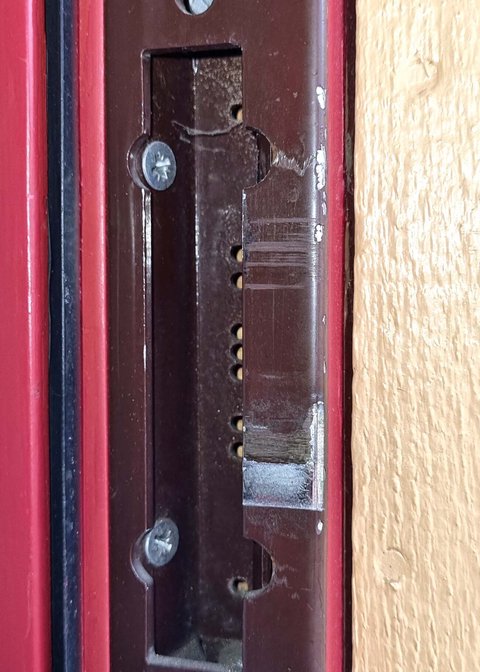 Primer plano de un cerradero metálico atornillado al marco de una puerta