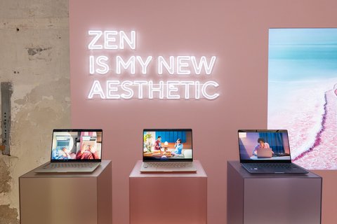 Tres ASUS Zenbook 14 de distintos colores sobre peanas rosas bajo un letrero de neón